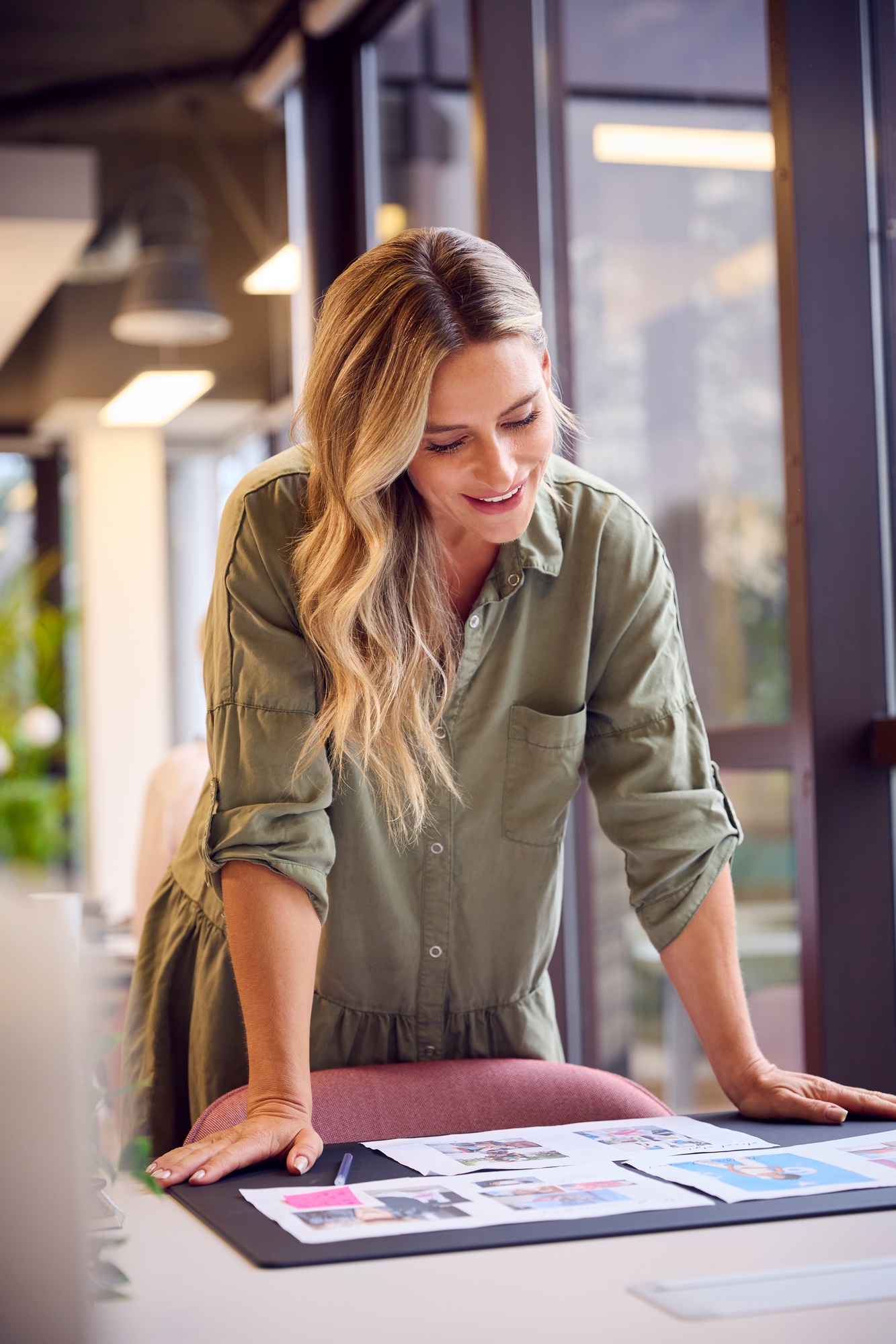 Businesswoman Standing At Desk In Open Plan Office Approving Or Checking Proofs Or Design Layouts