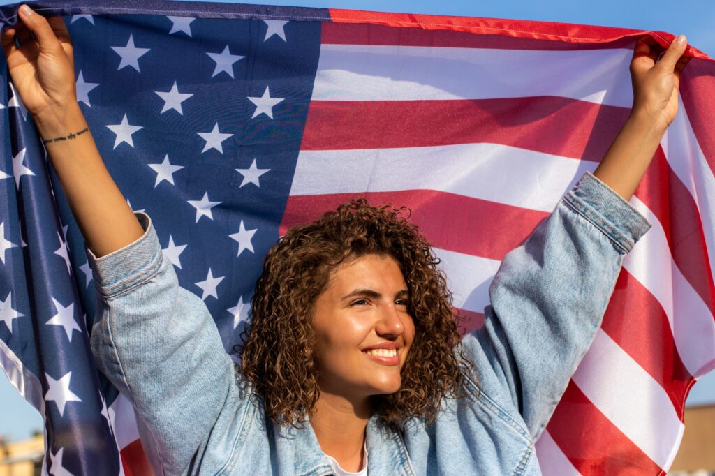Happy Beautiful diverse curly haired woman holding United States of America flag